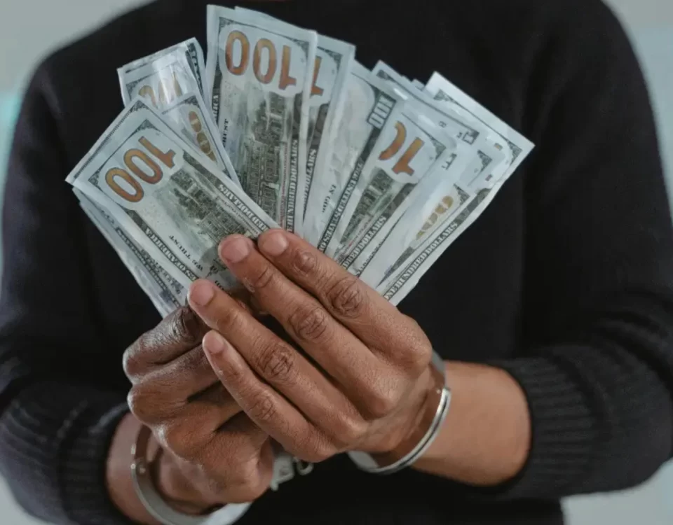 Kelepçeli ellerinde dolar banknotları tutan kişi; TCK 157 dolandırıcılık suçu, hileli menfaat temini ve ceza soruşturması temasını temsil eden görsel.