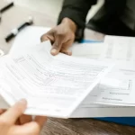 Re'sen Tarhiyat 2 Re’sen tarhiyat ve ceza ihbarnamesine itiraz sürecini anlatan görsel; masa üzerinde vergi evraklarının incelenmesi ve evrak teslimi.