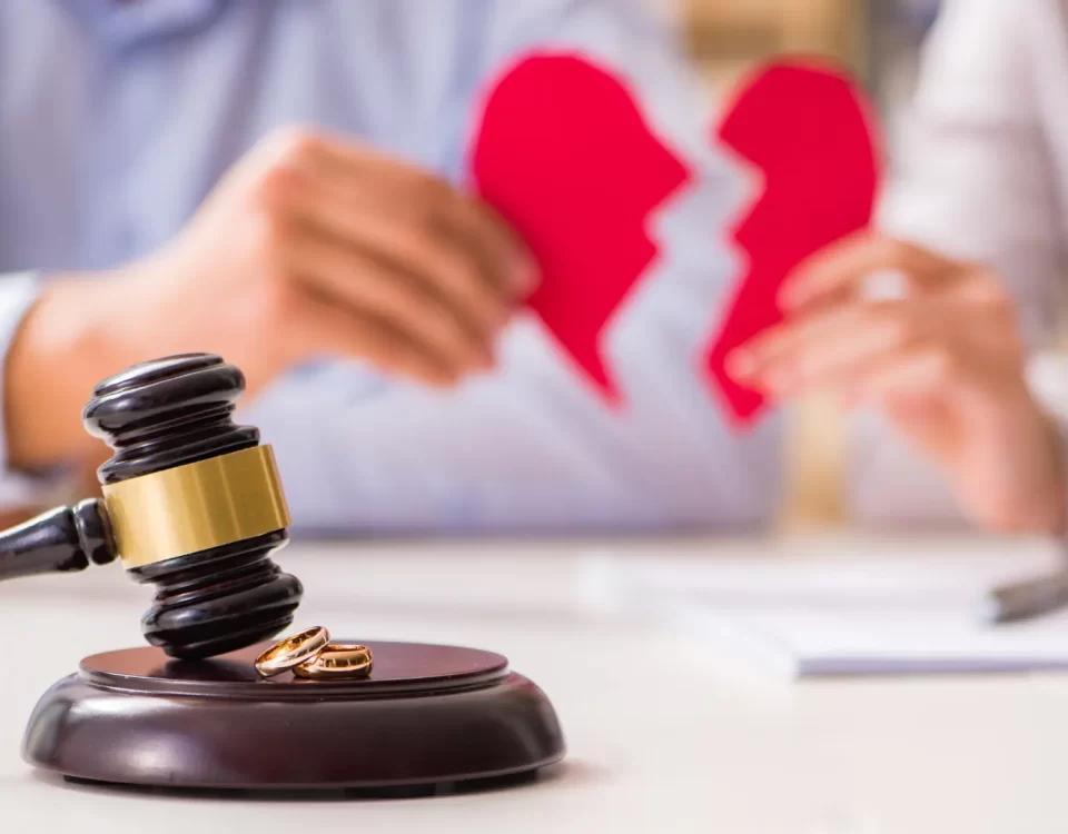 Mahkeme tokmağı ve alyansların yanında kırık kalp tutan çift; zina ve aldatma nedeniyle çekişmeli boşanma davası, manevi tazminat ve hukuki süreci temsil eden görsel.