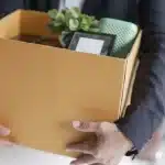 İşverenin Haklı Nedenle Derhal Fesih Hakkı: 4857 Sayılı İş Kanunu Kapsamında Hukuki Analiz 1 Haklı nedenle fesih süreci sonrasında kişisel ofis eşyalarını bir karton kutuya toplamış halde taşıyan takım elbiseli çalışan.