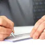 Karşılıksız Çek: İhtiyati Haciz, İcra Takibi ve Cezai Sorumluluk 1 Bir elinde gümüş renkli dolma kalemle ticari bir çek imzalayan veya karşılıksız çek keşide eden takım elbiseli iş insanı.