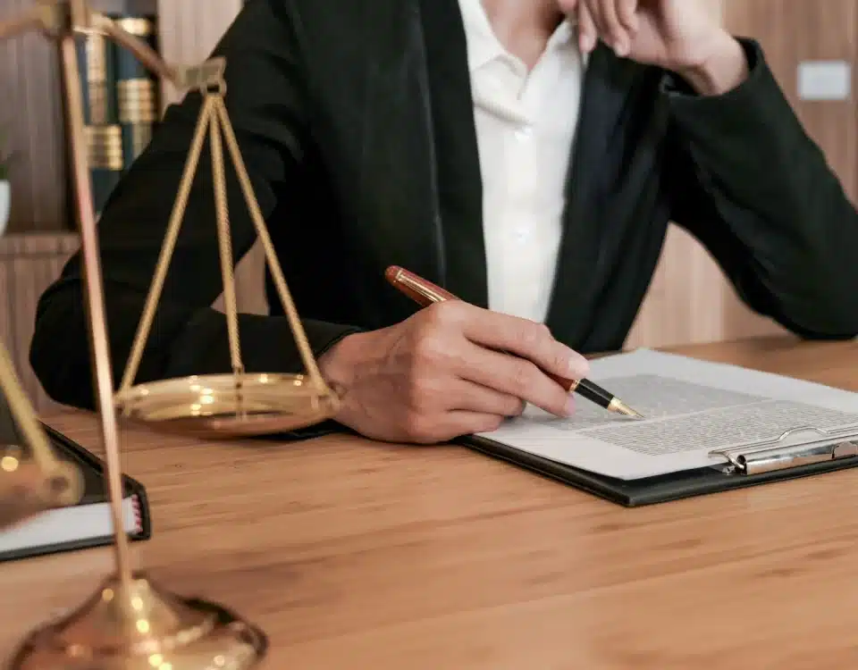 Masasında adalet terazisi bulunan bir hukukçunun veya tacirin, ticari sözleşmede cezai şart hükümlerini içeren hukuki belgeyi dikkatle incelemesi.