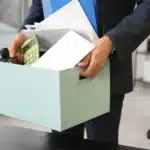 Kod 29 Nedir? Ahlak ve İyiniyet Kurallarına Aykırılık Nedeniyle Fesih 1 SGK işten çıkış bildiriminde Kod 29 ile işten çıkarma gerekçesiyle karşılaşan, kişisel eşya kutusunu taşıyan takım elbiseli bir çalışanın uğradığı hak kayıplarını ve haksız fesih sürecini sembolize eden kurumsal ofis görseli.