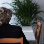 Ölüm Aylığı ve Dul-Yetim Aylığı Bağlanması: Şartlar, Oranlar ve Güncel Yargı Kararları 1 Vefat eden sigortalının geride kalan eş ve çocuklarına bağlanacak olan ölüm aylığı hak sahipliği durumunu ve dul aylığı başvuru sürecindeki yasal yas dönemini sembolize eden, evinde masada oturup pencereden dışarı bakan siyah elbiseli yalnız bir kadın ve arka planda çerçeveli taziye fotoğrafının yer aldığı kurumsal sosyal güvenlik hukuku görseli.
