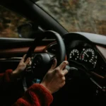 Alkollü Araç Kullanma Cezası ve Ehliyetin Geri Alınması (2026) 1 Karayolları Trafik Kanunu kapsamında belirlenen promil sınırının aşılması neticesinde uygulanan alkollü araç kullanma cezası, sürücü belgesinin geri alınması ve trafik güvenliğini tehlikeye sokma suçu yaptırımlarını sembolize eden, gece vakti hareket halindeki bir otomobilin direksiyonunu ve iç panel göstergelerini tutan sürücü elleri kurumsal hukuk görseli.