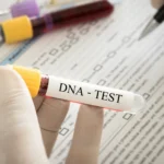 Babalık Davası ve DNA Testi 2 Evlilik dışı doğan çocuğun biyolojik babası ile soybağının kurulması amacıyla açılan babalık davası sürecini, mahkeme kararıyla Adli Tıp Kurumu tarafından yürütülen kan ve DNA profil incelemelerini sembolize eden; tıbbi laboratuvarda elinde "DNA - TEST" yazılı kan tüpü tutan eldivenli bir tıp uzmanını ve arka plandaki tıbbi evrakları gösteren kurumsal hukuk görseli.