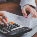 Çifte Vergilendirmeyi Önleme Anlaşması ve Yurt Dışı Kazançların Beyanı 2 Uluslararası iki taraflı vergi anlaşmaları uyarınca yurt dışı kaynaklı gelirlerin Türkiye'deki vergi yükümlülüklerini hesaplayan ve çifte vergilendirmeyi önleme anlaşması hükümlerine göre mahsup edilecek tutarları belirleyen; masasında resmi yabancı ve yerli vergi beyannamesi formları bulunan, elinde kalemle hesap makinesinde işlem yapan kurumsal bir uluslararası vergi avukatı veya mali danışman figürü.