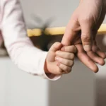 Çocukla Kişisel İlişki Düzenlemesi: Şartları, Süreci ve Güncel Yargıtay Kararları 2 Boşanma veya ayrılık süreci sonrasında velayet hakkı kendisine verilmeyen ebeveynin çocukla kişisel ilişki kurma hakkını, ebeveynlik bağlarının korunmasını ve çocukla geçirilen görüşme zamanlarını sembolize eden; küçük bir çocuğun bir yetişkinin elini sevgiyle tuttuğu kurumsal aile hukuku görseli.