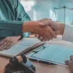 Kira Sözleşmesinde Kefilin Sorumluluğu 2 Masa üzerinde duran resmi sözleşme, hakim tokmağı ve adalet terazisi eşliğinde tokalaşan iki kişi; Nişantaşı bölgesindeki kira sözleşmesinde kefilin sorumluluğu ve hukuki mutabakat sürecini temsil eder.