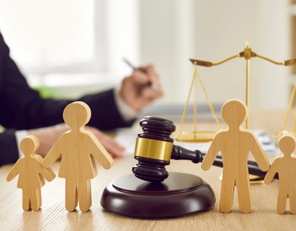 Velayetin Değiştirilmesi Davası: 2026 Kapsamlı Rehber 10 Bir hukuk ofisinde veya mahkeme salonunda, arka planda adalet terazisi ve evrak imzalayan hukukçu silüetinin önünde yer alan, ebeveyn ile çocuk ilişkilerini ve yasal ayrılık süreçlerini simgeleyen ahşap figürler ile ortadaki hâkim tokmağını gösteren, velayetin değiştirilmesi davası ve velayet hakkının kötüye kullanılması konularıyla ilgili kurumsal aile hukuku görseli.