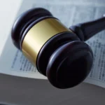 Vesayet Davası ve Kısıtlama Şartları 2 Akıl hastalığı, yaşlılık veya savurganlık gibi nedenlerle kendi işlerini göremeyecek durumda olan kişilere vasi atanması amacıyla açılan vesayet davası sürecini ve bu doğrultuda verilen mahkeme kısıtlama kararlarını sembolize eden; açık bir kanun kitabı (hukuk mevzuatı) üzerinde duran ahşap ve pirinç detaylı bir hakim tokmağını yakından gösteren kurumsal hukuk görseli.
