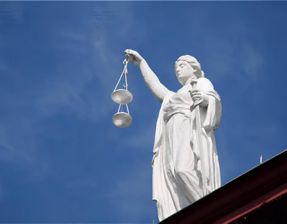 Mavi gökyüzü önünde terazi ve kılıç tutan beyaz adalet heykeli; İstanbul'da iş kazası geçiren işçilerin adliye koridorlarındaki hak arayışını ve iş kazası tazminatı davalarındaki hukuki süreci temsil eder.