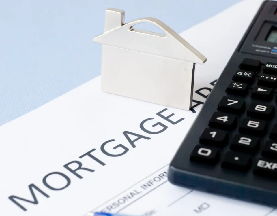 Üzerinde mortgage yazılı sözleşme evrakı, ev maketi ve hesap makinesi; İstanbul'daki bankalardan kullanılan konut kredisi erken kapama hesaplamalarını ve kalan anapara üzerinden yapılan faiz indirimini temsil eder.