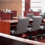 Ahşap masaları, mikrofonları ve gri koltuklarıyla boş bir duruşma salonu; İstanbul mahkemelerinde mağdurun yaşadığı acıya göre hakimin takdir yetkisiyle belirlenen manevi tazminat miktarı karar süreçlerini temsil eder.