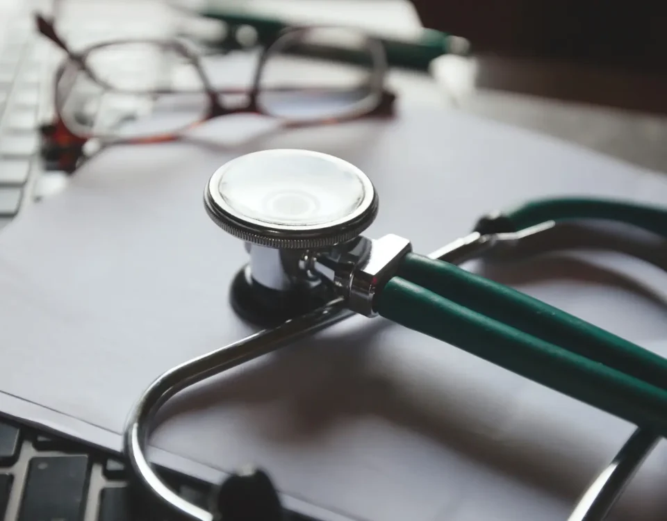 Dizüstü bilgisayar klavyesi ve boş evrak üzerinde duran steteskop ile gözlük; İstanbul'daki hastanelerde yaşanan doktor hatalarını ve tıbbi malpraktis tazminat davası süreçlerindeki tıbbi kayıt (epikriz) incelemelerini temsil eder.